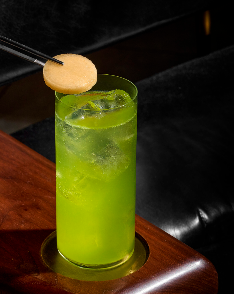 Vibrant green iced cocktail in a highball glass garnished with a melon slice