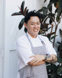 Smiling chef in white uniform and grey apron standing outside Po Restaurant