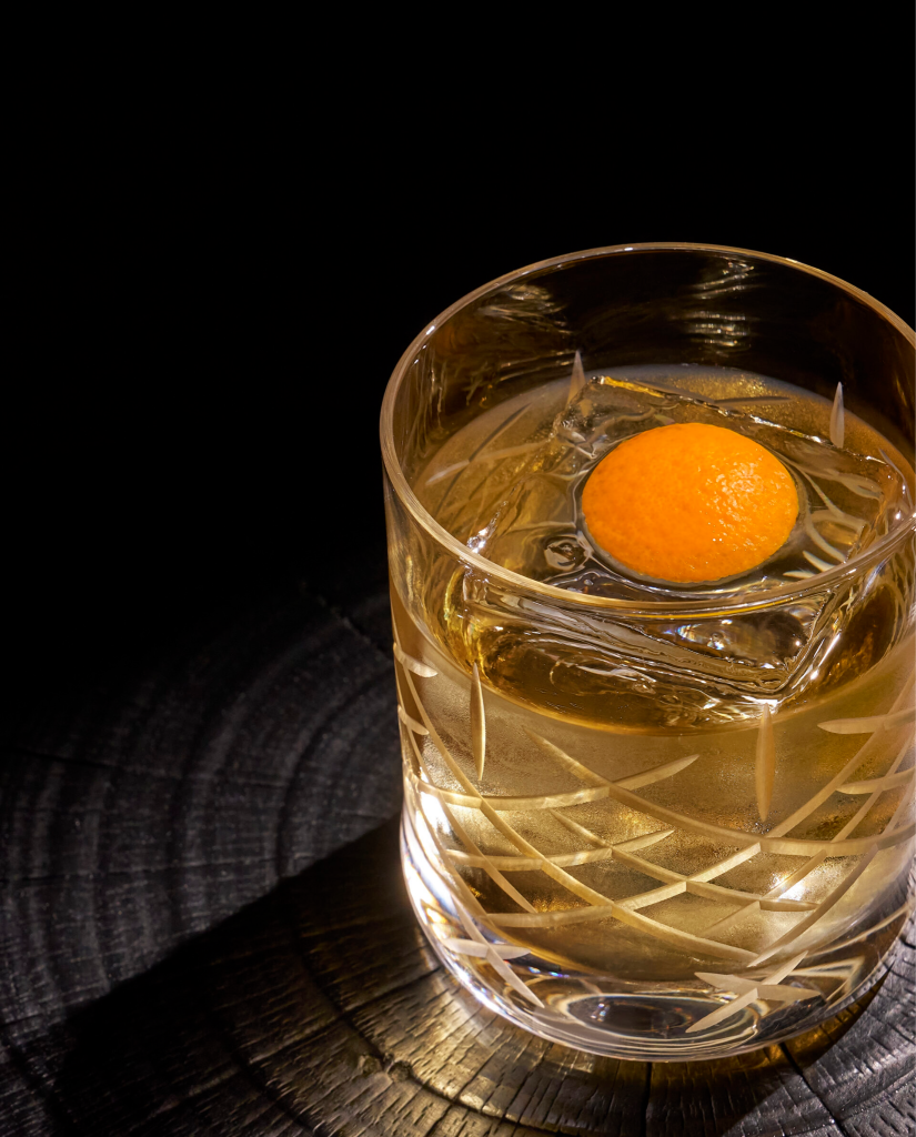Old Fashioned whiskey cocktail in a crystal rocks glass with clear ice and orange peel
